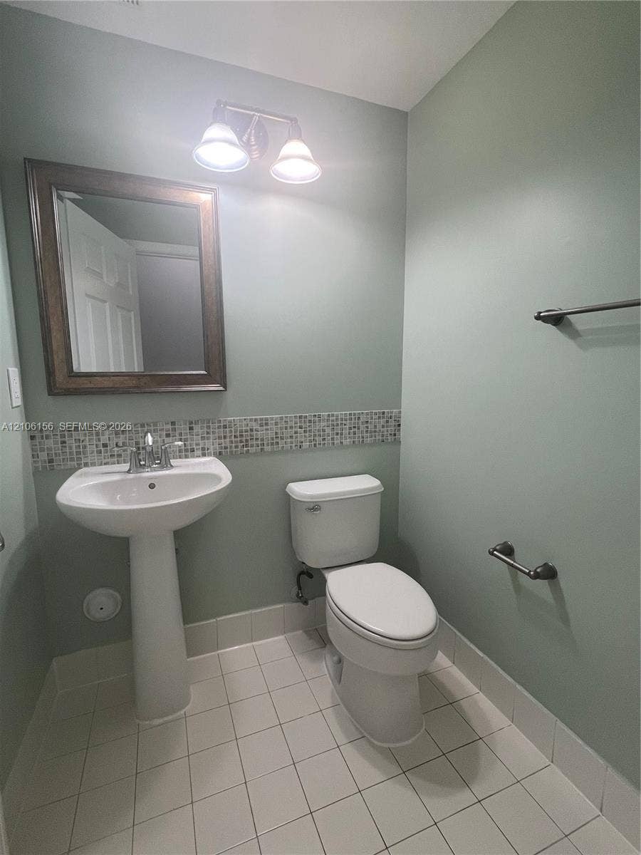 Pedestal sink with chrome faucet, wall-mounted mirror with wood-finish frame, mosaic tile backsplash, dual-light vanity fixture, and tiled flooring