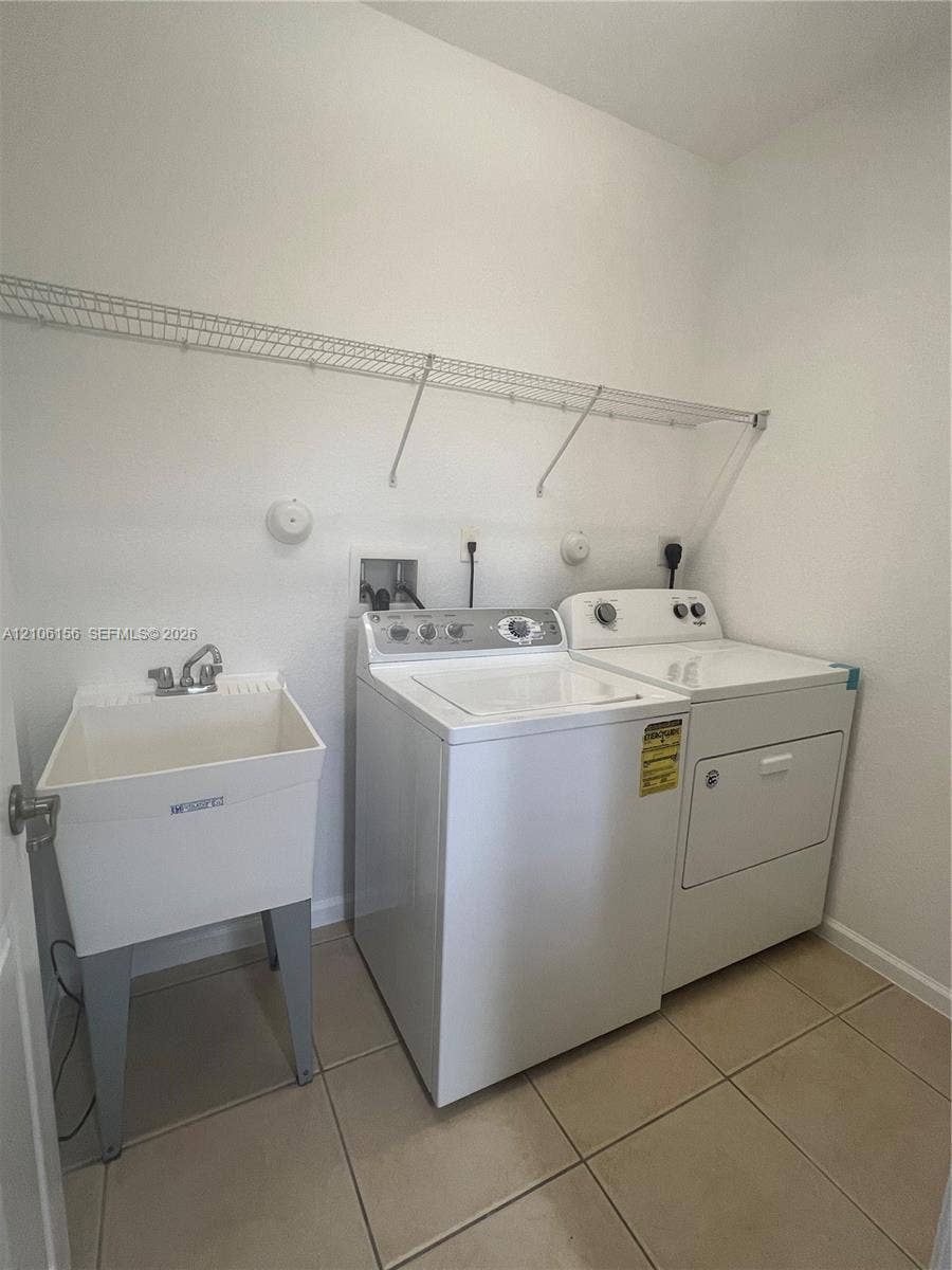 Laundry area featuring ceramic tile flooring, a utility sink with a chrome faucet, and wire wall shelving
