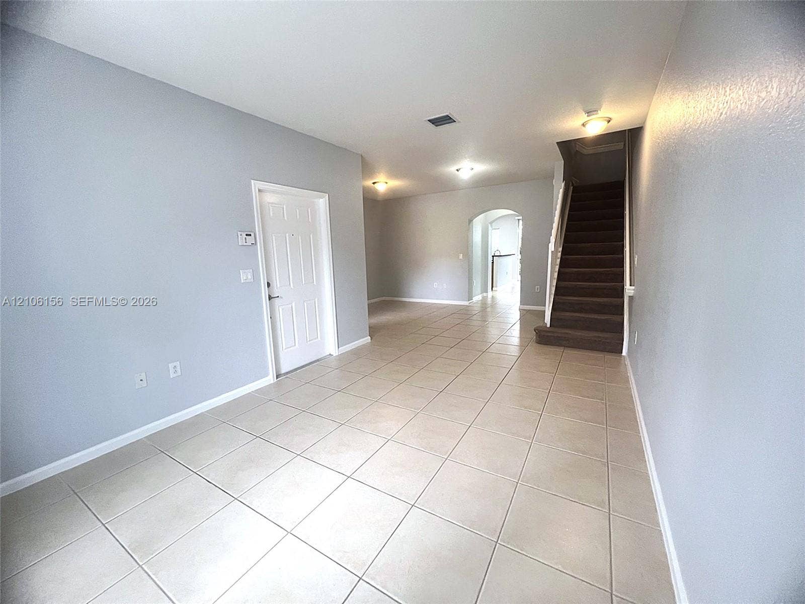 Ceramic tile flooring, neutral wall tones, arched architectural detailing, and a carpeted staircase with white balusters