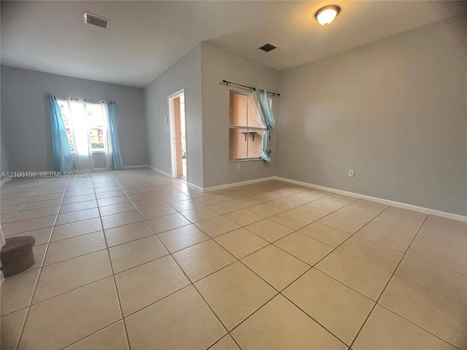 Interior space featuring light-toned tile flooring, neutral wall paint, and multiple windows providing natural light