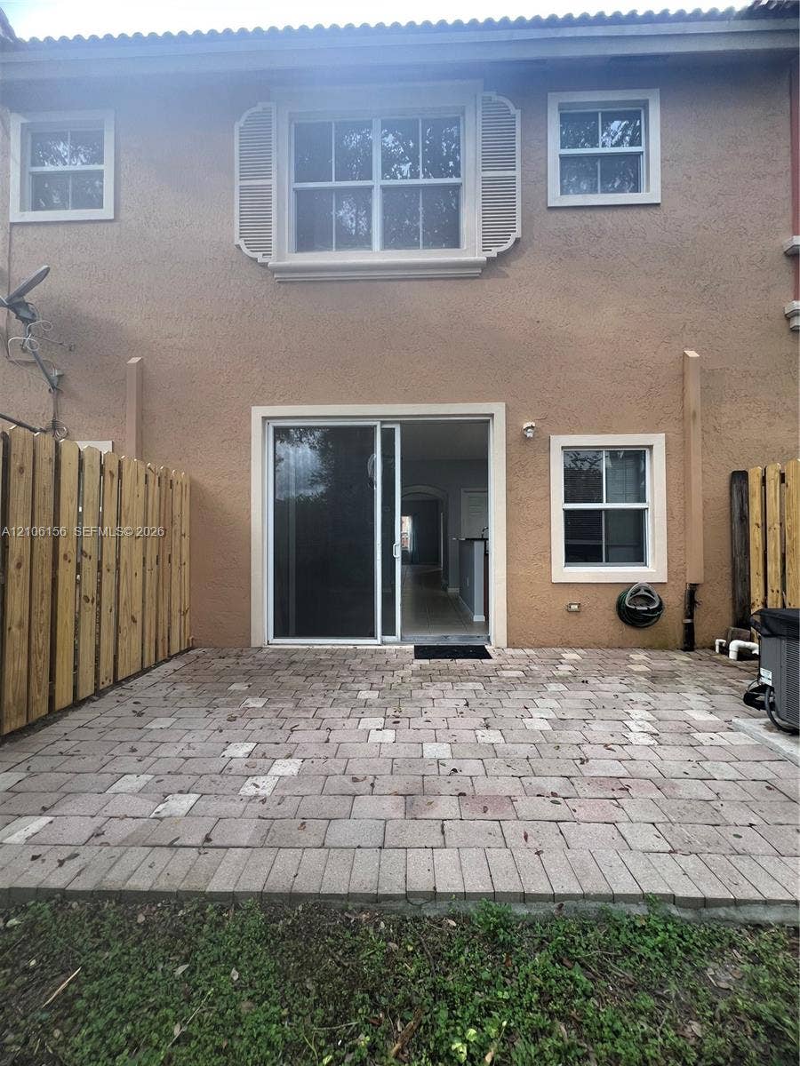 Rear exterior featuring a paved stone patio, dual-sided wood privacy fencing, sliding glass door, and exterior windows with decorative shutters