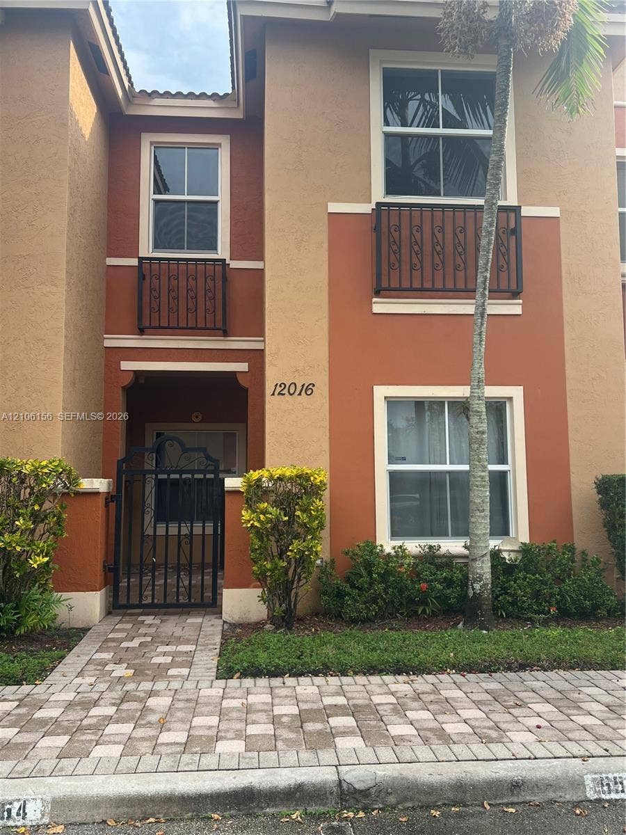 Stucco exterior featuring dual Juliet balconies with decorative iron railings, arched entryway, and a paver stone walkway