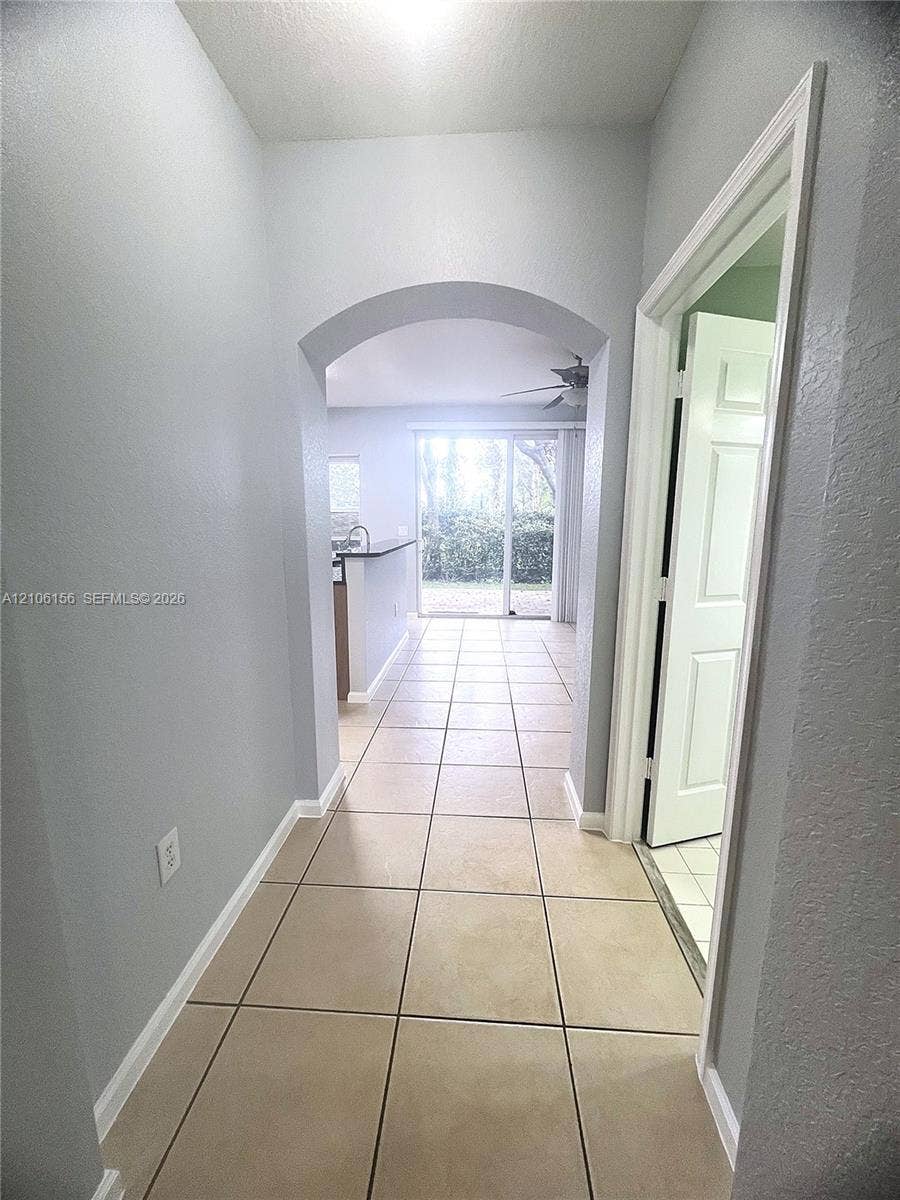 Hallway featuring ceramic tile flooring, arched architectural opening, and a multi-panel interior door