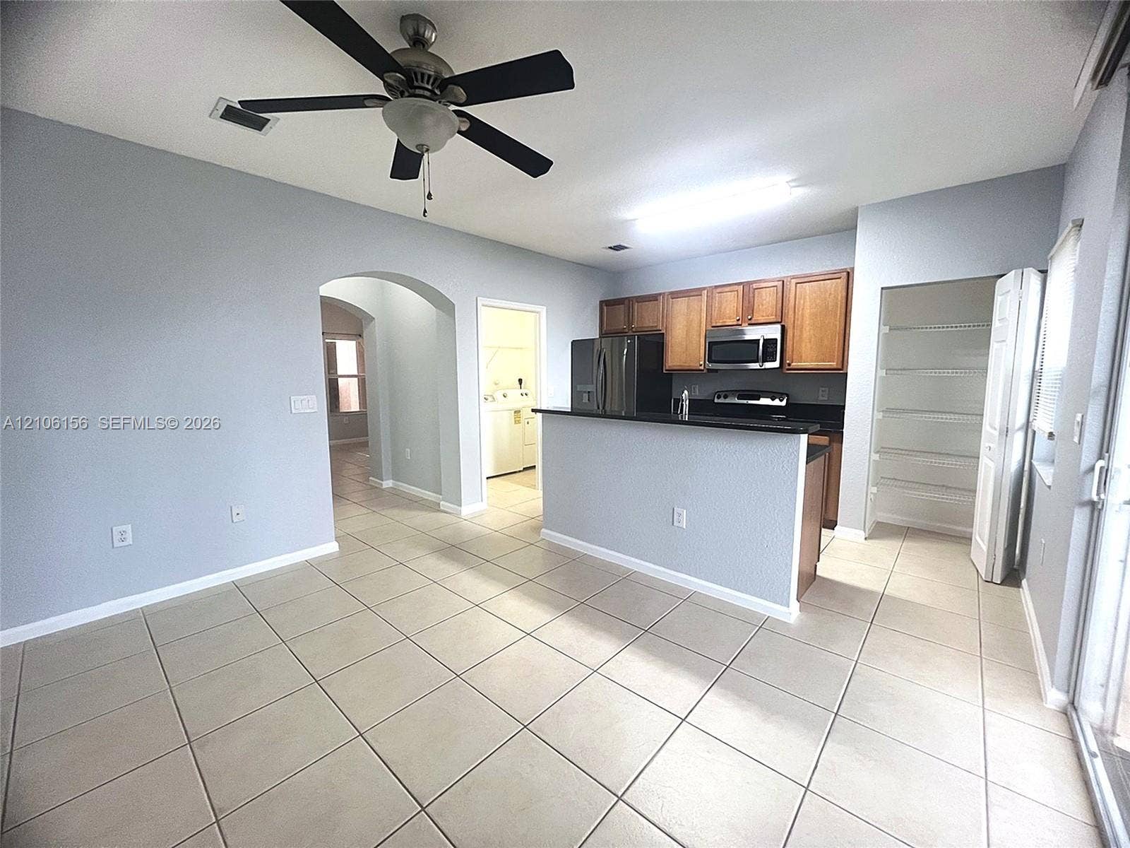 Kitchen featuring wood cabinetry, solid-surface countertops, built-in stainless steel microwave, and tile flooring
