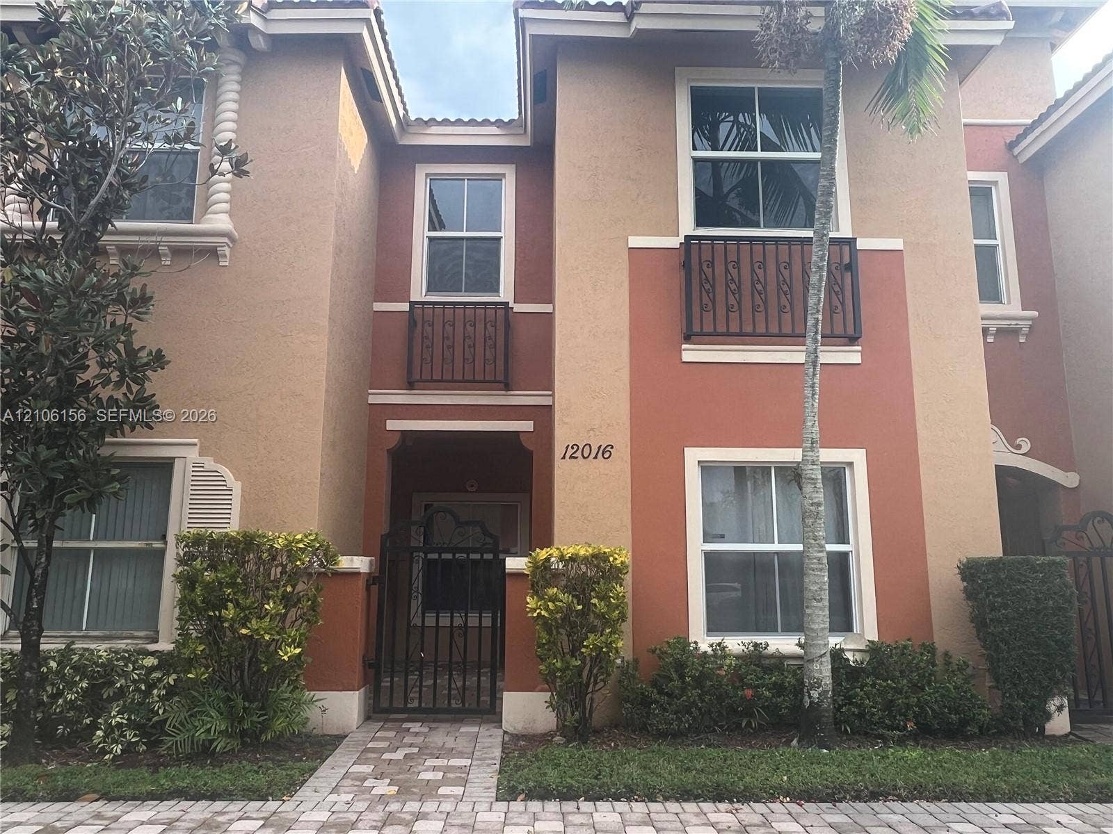 Stucco exterior featuring dual wrought-iron Juliet balconies, arched entry detailing, decorative corbel accents, and a paver stone walkway