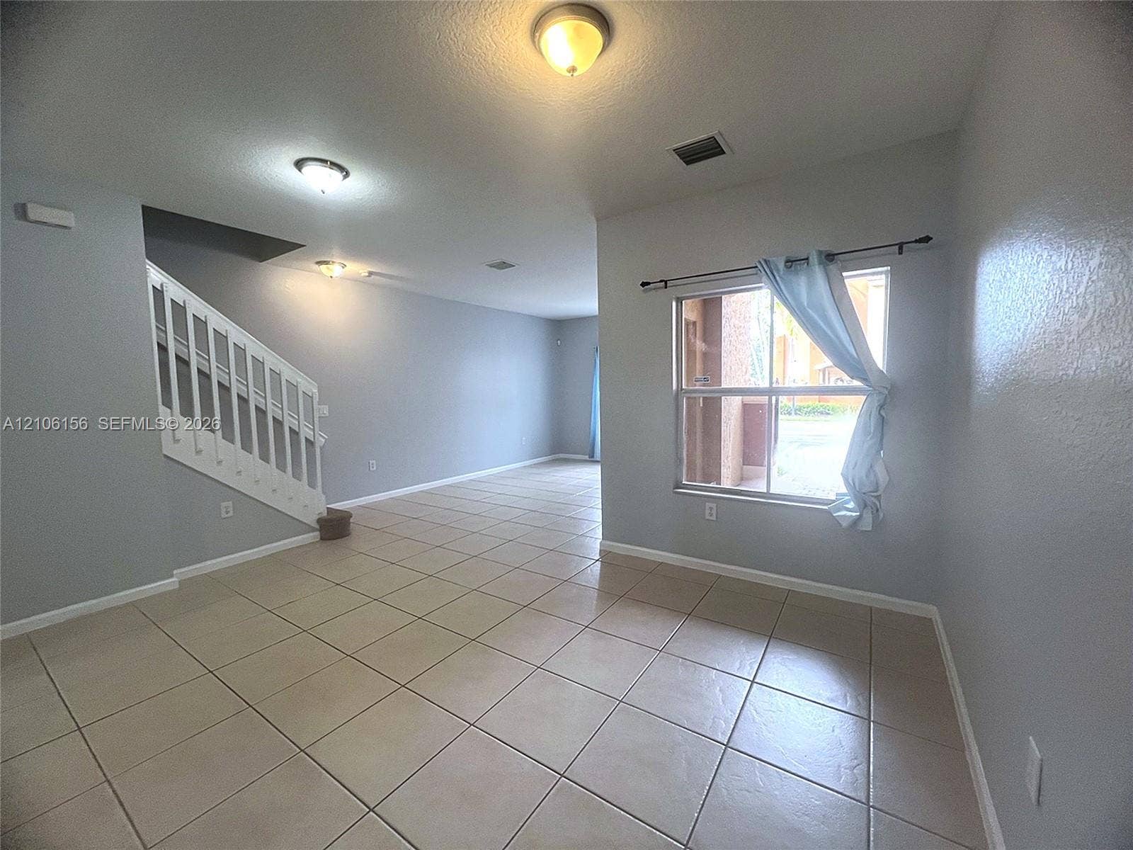 Neutral-toned interior featuring ceramic tile flooring, a staircase with white wooden balustrades, and natural light from a single-pane window