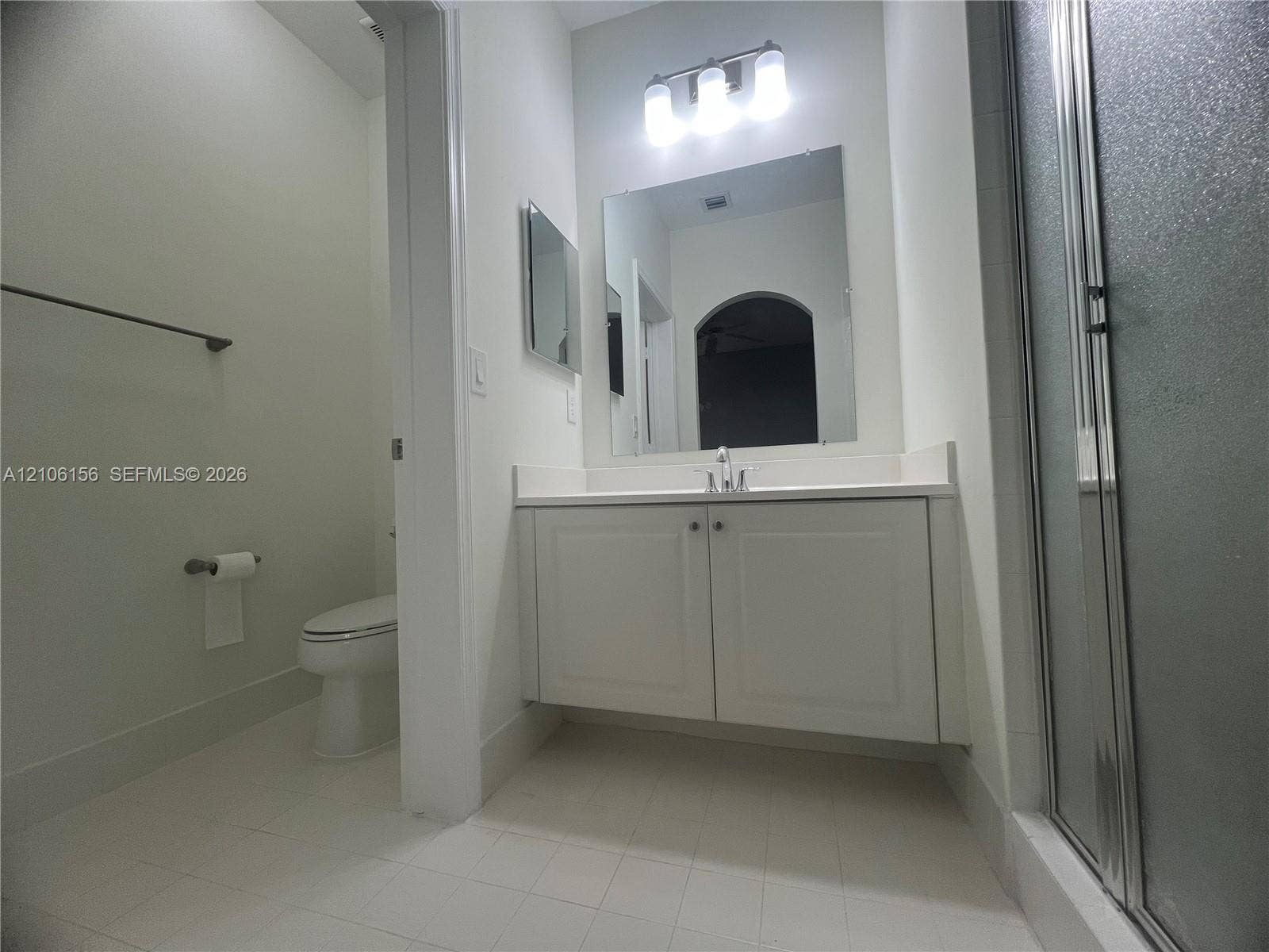 Floating vanity with white cabinetry and solid-surface countertop, rectangular wall mirror, three-bulb vanity lighting, and walk-in shower enclosure