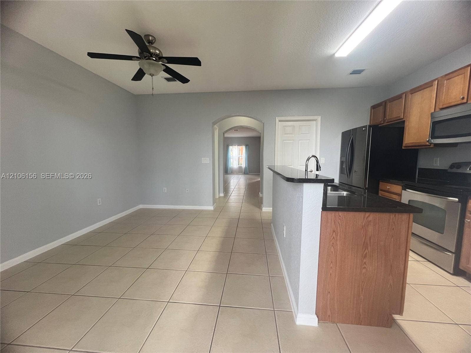 Kitchen featuring a stone-surface breakfast bar, wood cabinetry, stainless steel appliances, tile flooring, and a ceiling fan