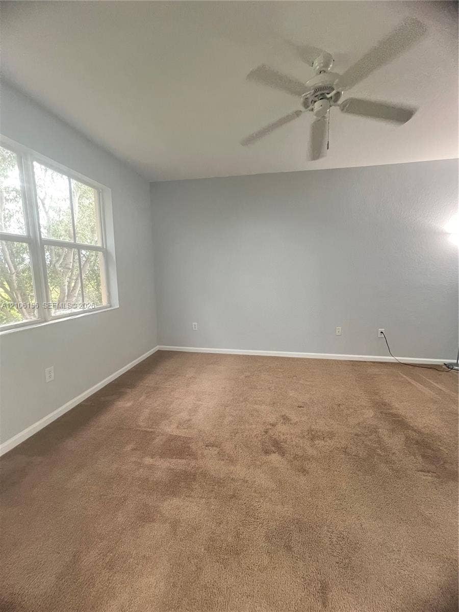 Neutral wall finish featuring a multi-pane window, carpeted flooring, and a ceiling fan with integrated lighting