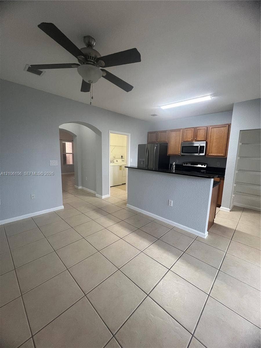 Kitchen area featuring wood cabinetry, a breakfast bar with dark countertops, stainless steel appliances, ceramic tile flooring, and a ceiling fan