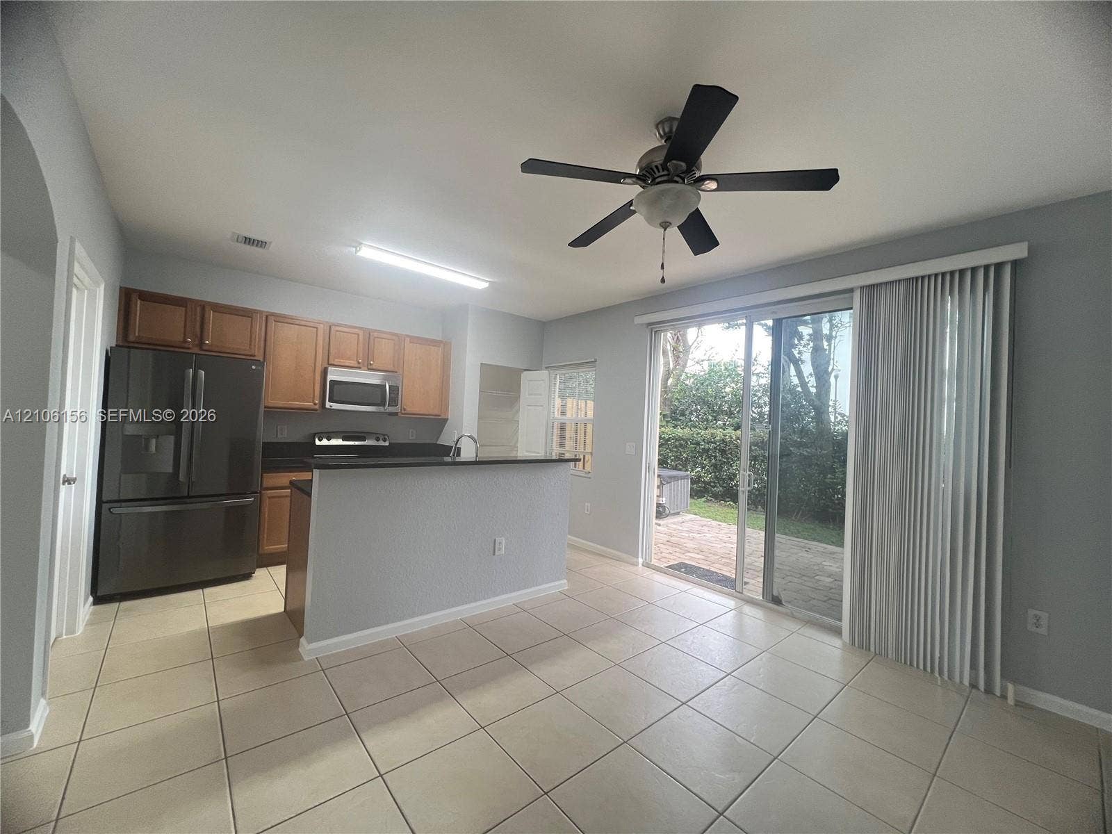 Kitchen featuring wood cabinetry, dark-toned countertop, stainless steel appliances, tile flooring, and sliding glass doors