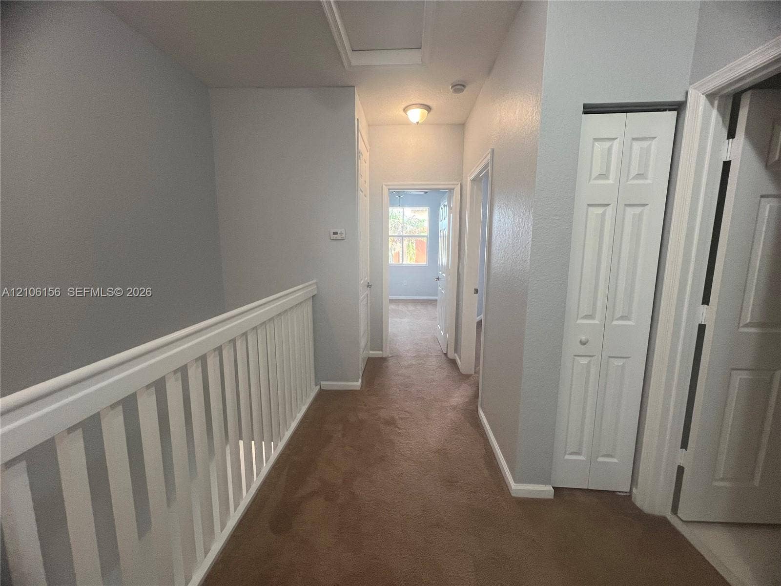 Hallway featuring neutral carpet flooring, white paneled interior doors, and a white balustrade with a horizontal handrail