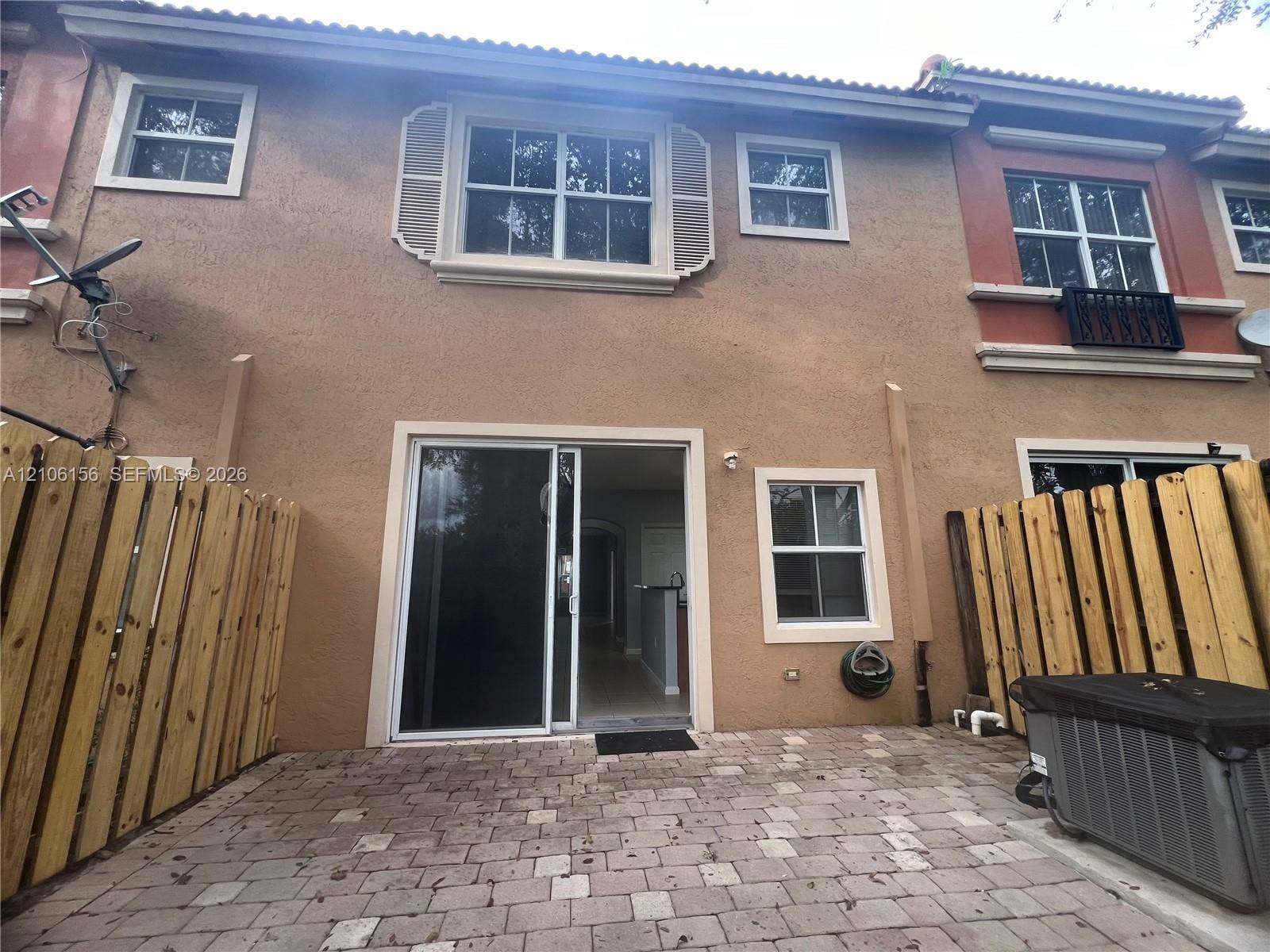 Stucco exterior featuring sliding glass doors, a paver patio, wood-style privacy fencing, and double-hung windows with decorative shutters