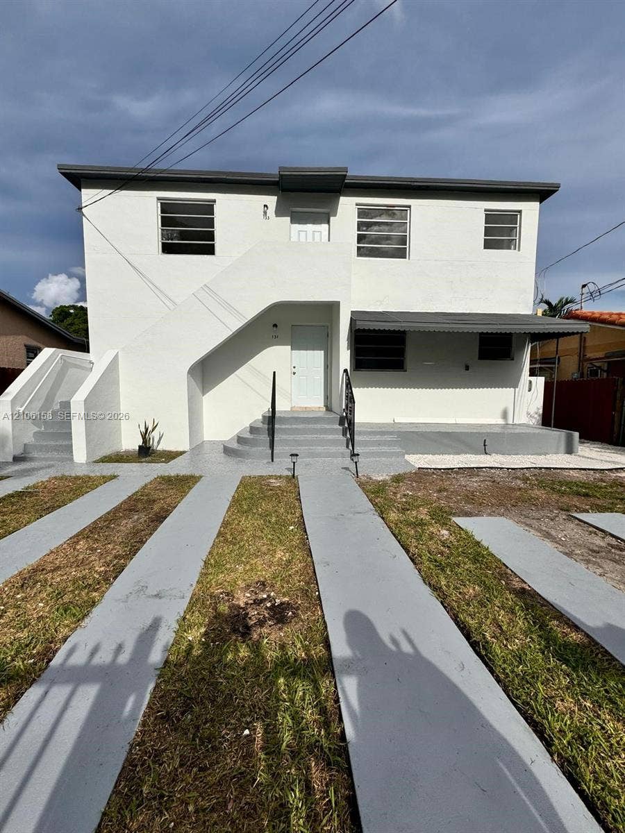 Two-story exterior featuring white stucco finish, multi-pane horizontal windows, metal awning, concrete front steps with metal railing, and concrete driveway strips