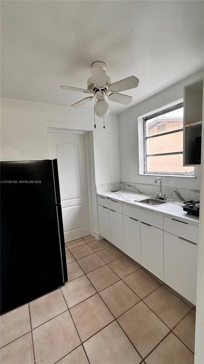 Kitchen featuring flat-panel white cabinetry, stone-patterned backsplash, square tile flooring, and ceiling fan with integrated lighting