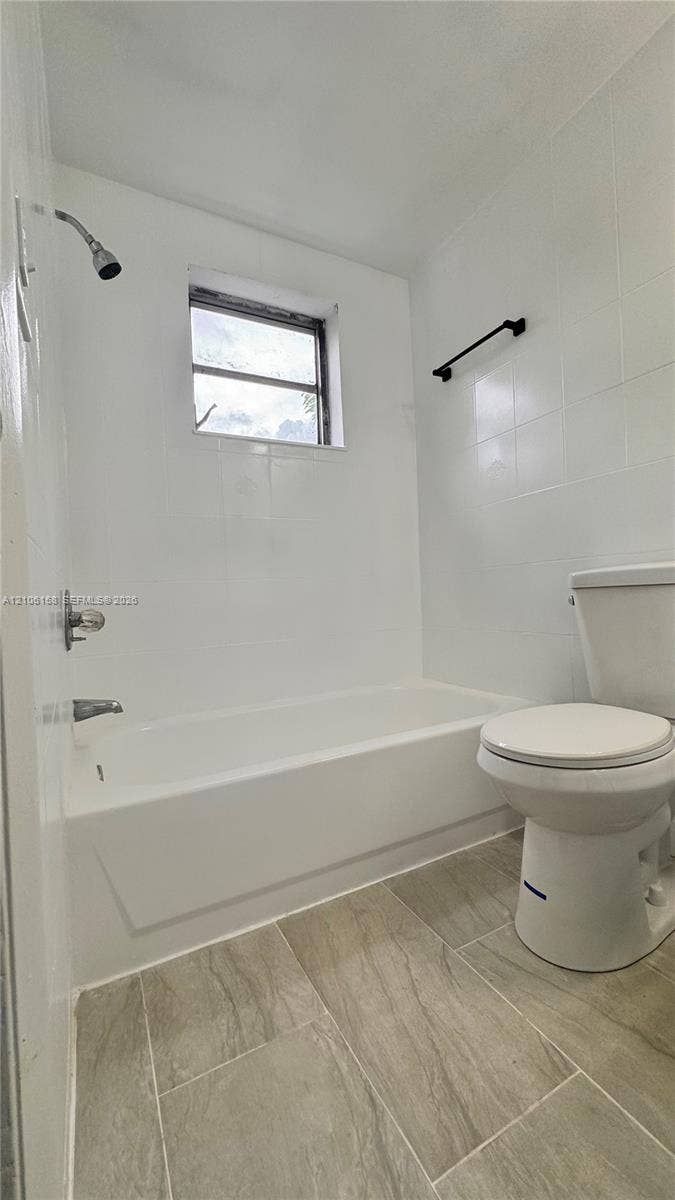 Bathroom featuring white wall tiling, a built-in tub with a shower head, ceramic tile flooring, and a matte black towel bar