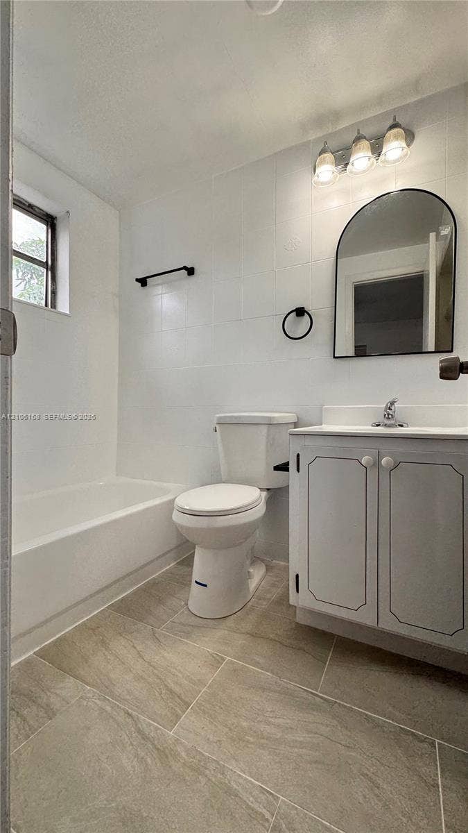 Bathroom featuring tile flooring, a white vanity cabinet with a neutral countertop, an arched wall-mounted mirror, and a three-light vanity fixture