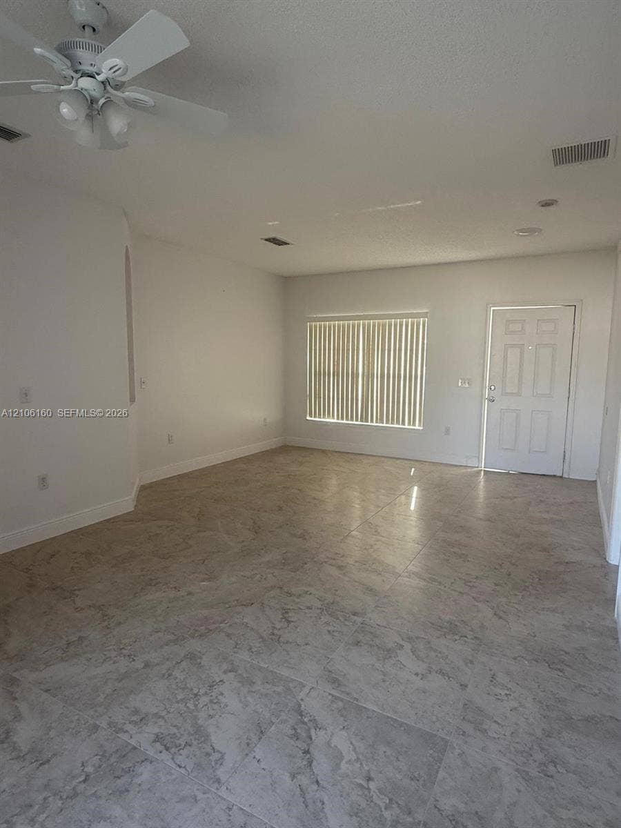 Neutral-toned tile flooring, ceiling fan with integrated lighting, and vertical window blinds