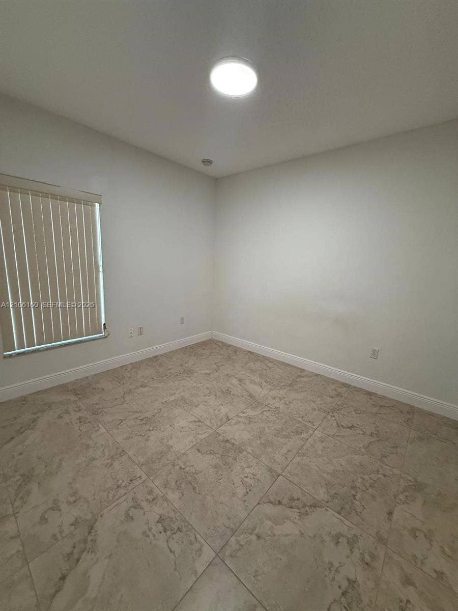Neutral interior space featuring stone-style tile flooring, a window with vertical blinds, and a flush-mount ceiling light fixture