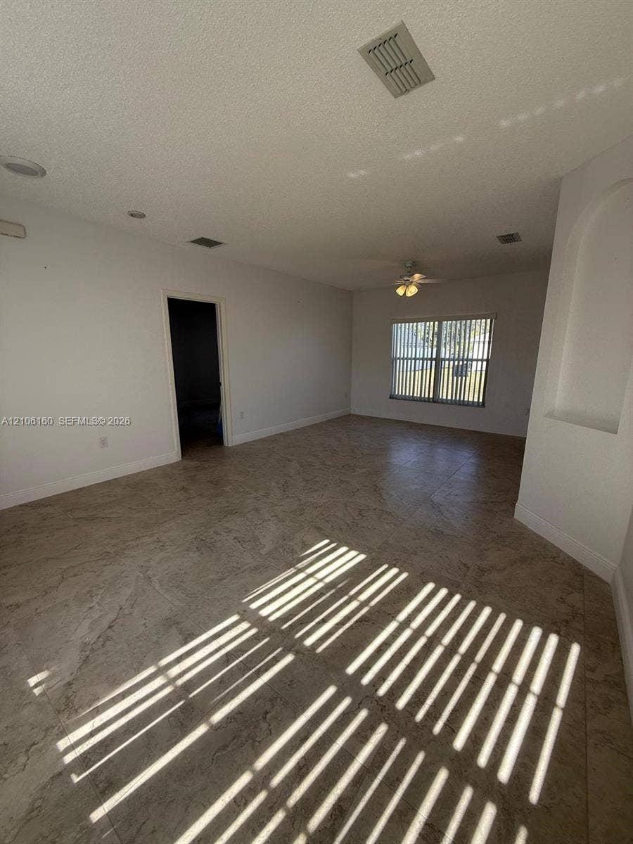 Open-concept interior featuring large-format tile flooring, recessed ceiling lighting, a ceiling fan with integrated light fixture, and an arched architectural wall niche