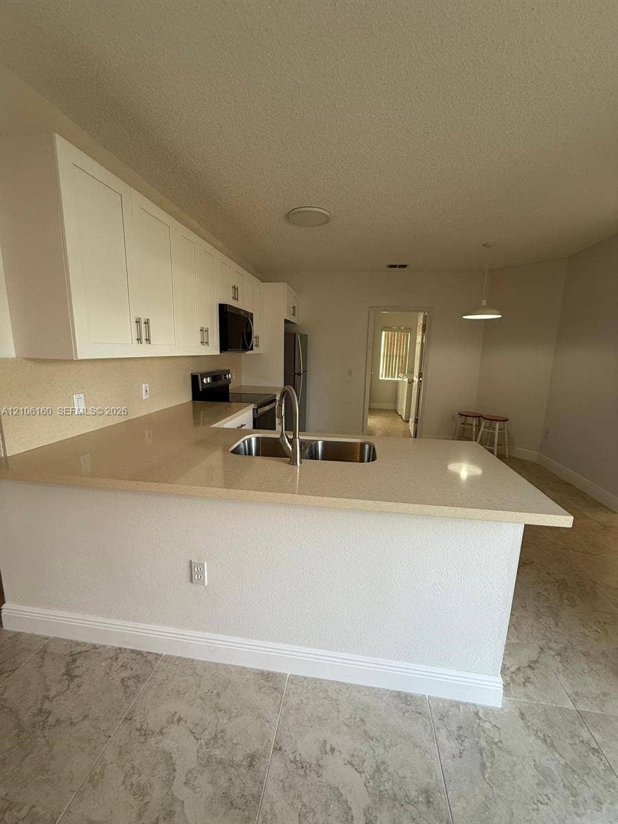 Kitchen featuring white cabinetry, solid-surface countertops, dual-basin stainless steel sink with gooseneck faucet, and tile flooring