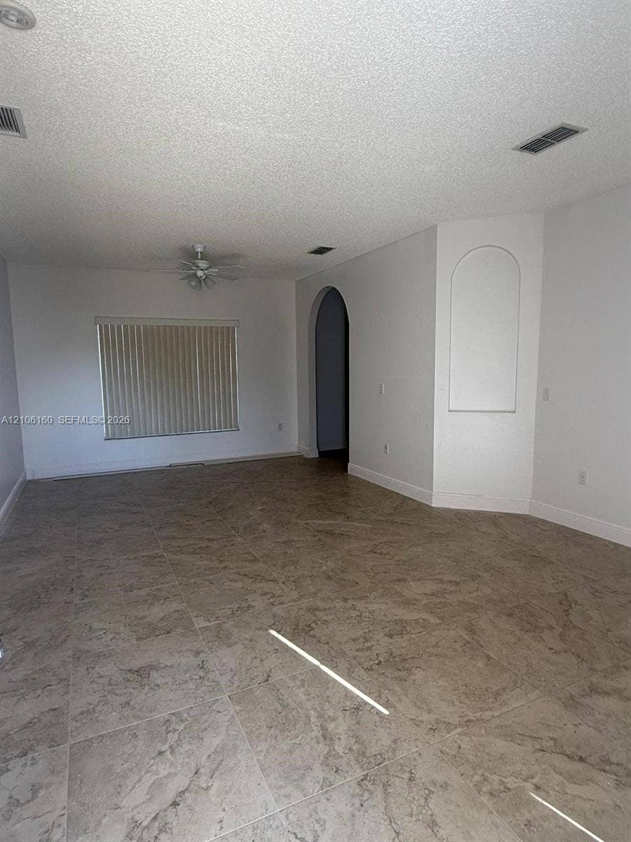 Interior space featuring neutral-toned tile flooring, an arched entryway, a built-in recessed wall niche, and a ceiling fan