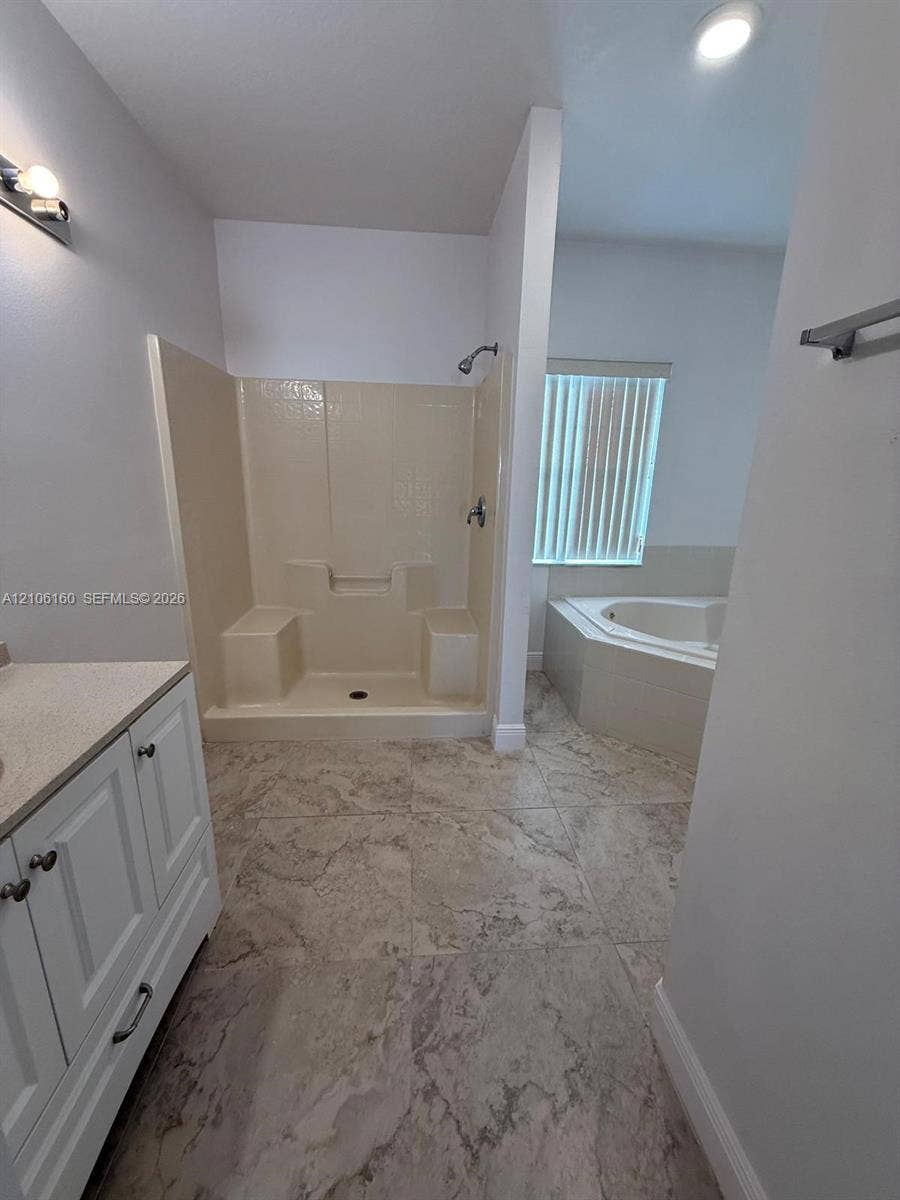 Bathroom featuring stone-finish floor tiling, white cabinetry with a stone-top vanity, an integrated walk-in shower stall, and a built-in jetted corner tub