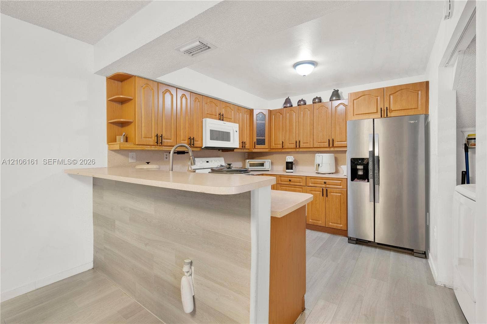 15460 SW 82nd Lane, #403, Miami, Miami, FL 33193 Kitchen featuring wood cabinetry, breakfast bar with wood-finish paneling, laminate countertops, stainless steel side-by-side refrigerator, and wood-finish flooring