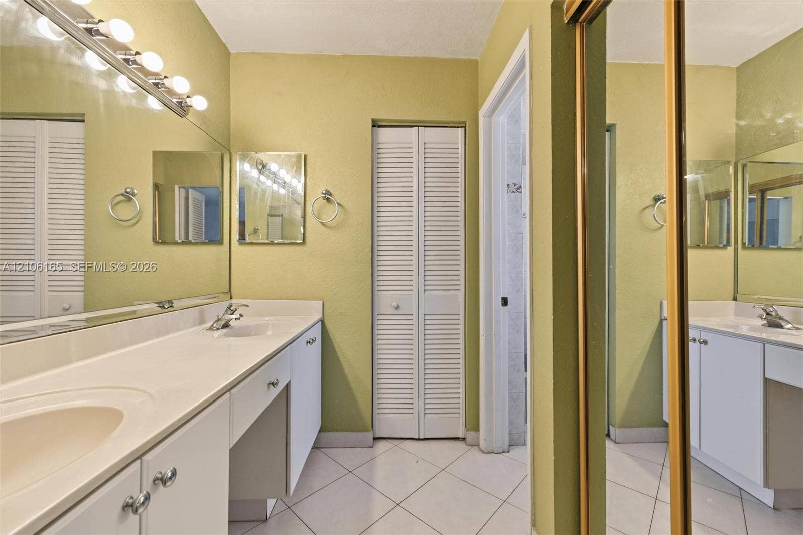 7205 W 3rd Avenue, #1, Hialeah, Hialeah, FL 33014 Bathroom featuring a dual-sink vanity with a solid-surface countertop, full-width vanity mirror, tile flooring, and louvered bifold closet doors