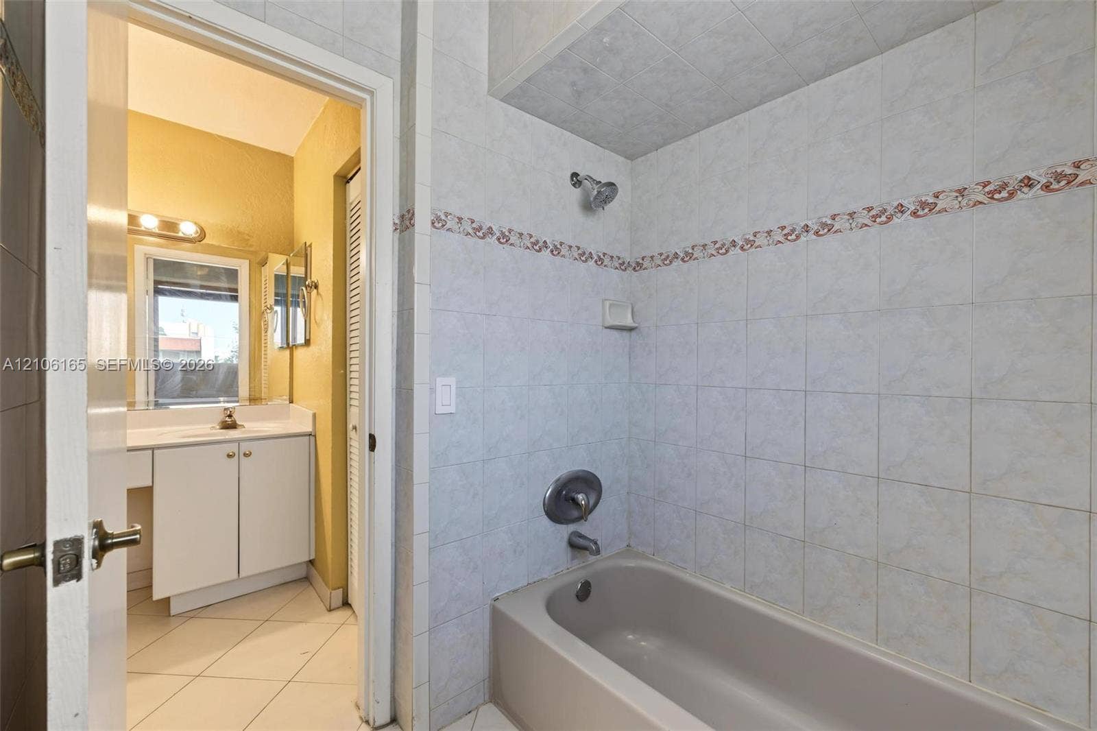 7205 W 3rd Avenue, #1, Hialeah, Hialeah, FL 33014 Bathroom featuring a tub and shower combination with light-toned wall tile, a white vanity cabinet with a solid surface countertop, louvered closet doors, and ceramic tile flooring