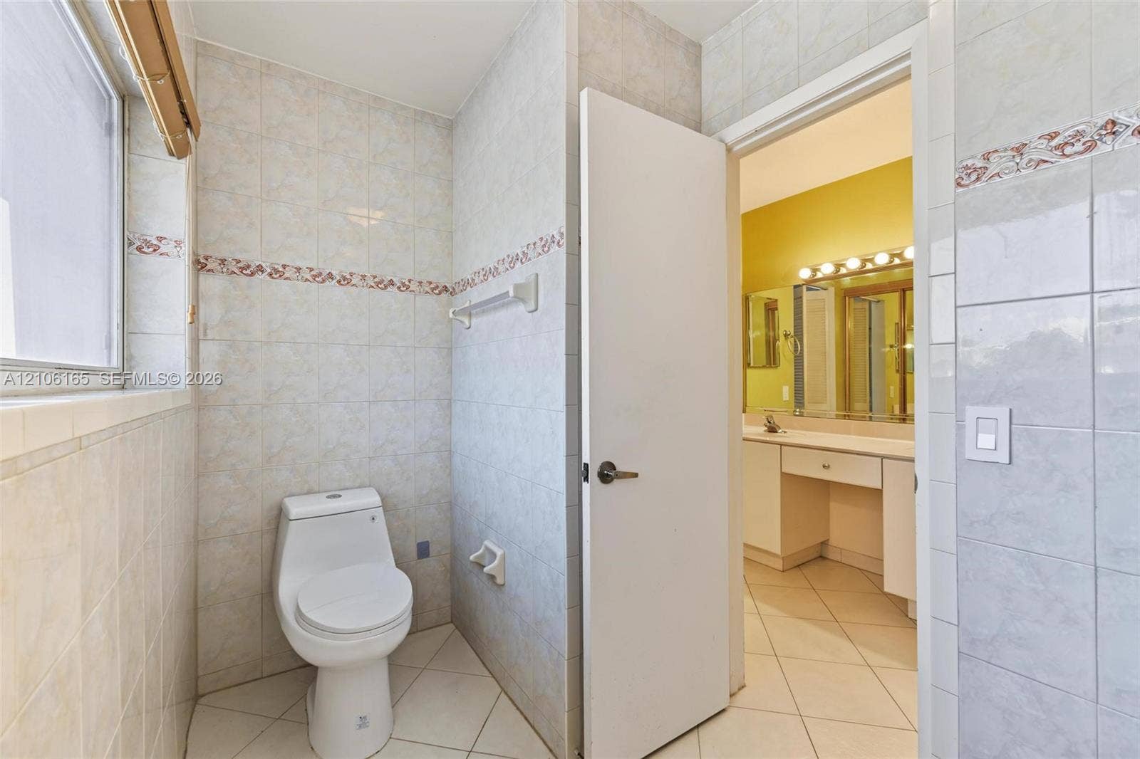 7205 W 3rd Avenue, #1, Hialeah, Hialeah, FL 33014 Bathroom featuring full-height ceramic tile walls with decorative border inlay, porcelain floor tile, white toilet, and built-in vanity with integrated lighting