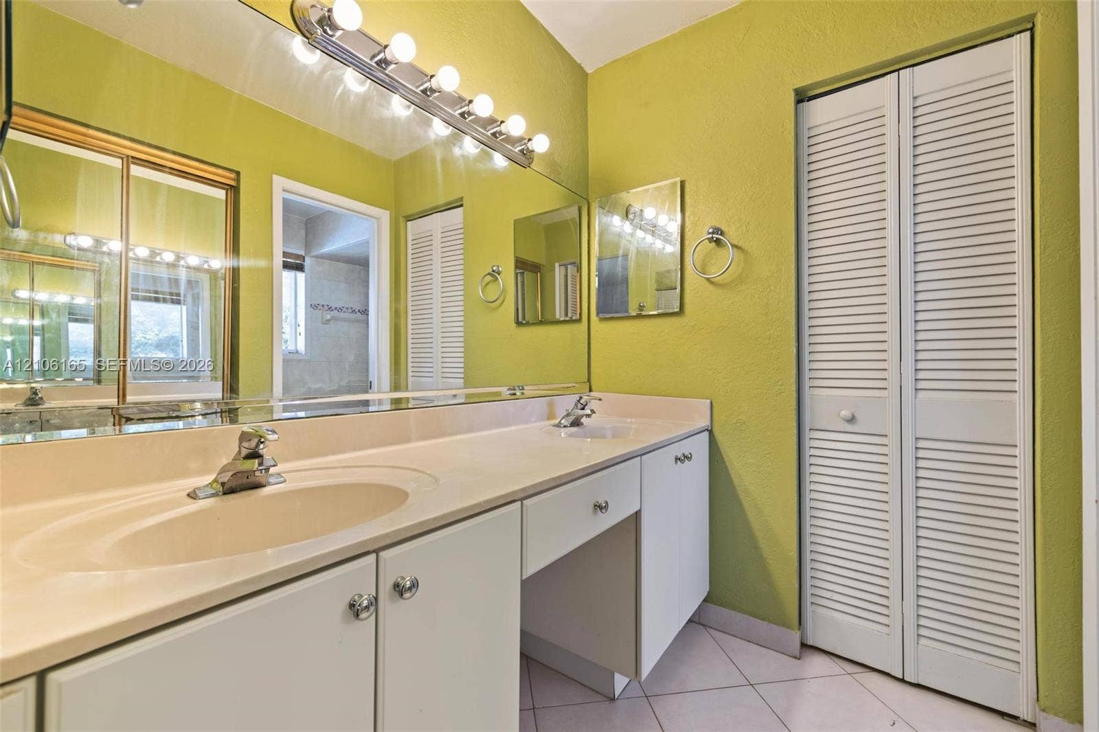 7205 W 3rd Avenue, #1, Hialeah, Hialeah, FL 33014 Dual-sink vanity with a solid-surface countertop, full-width wall mirror, integrated lighting fixture, and white louvered closet doors