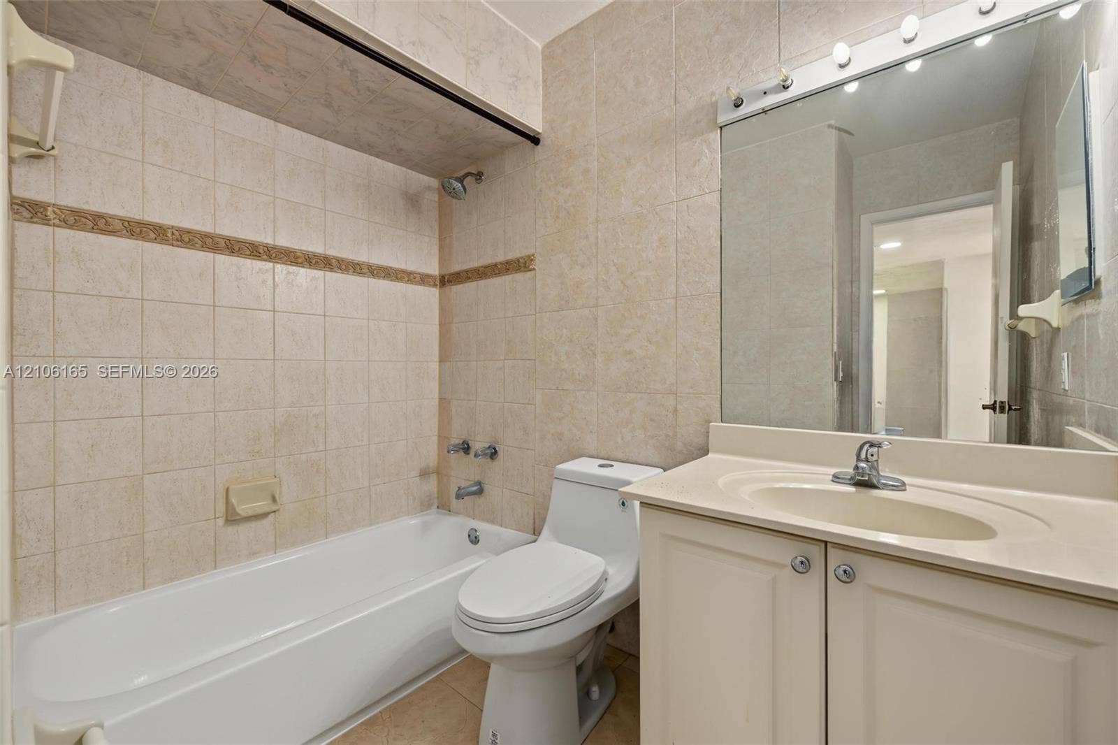 7205 W 3rd Avenue, #1, Hialeah, Hialeah, FL 33014 Bathroom featuring a white integrated vanity sink, tile-surround bathtub with shower head, neutral-toned wall tiling with decorative border, and a wall-mounted vanity mirror