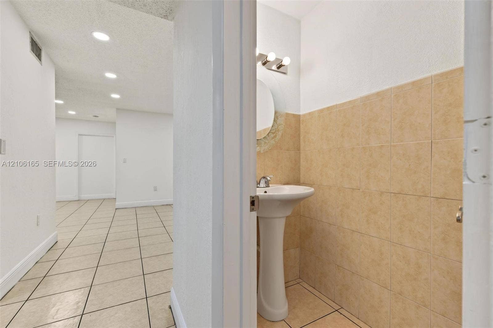 7205 W 3rd Avenue, #1, Hialeah, Hialeah, FL 33014 Ceramic tile flooring, pedestal sink with metal fixtures, circular vanity mirror, wall-mounted multi-light fixture, and ceramic tile wall accents
