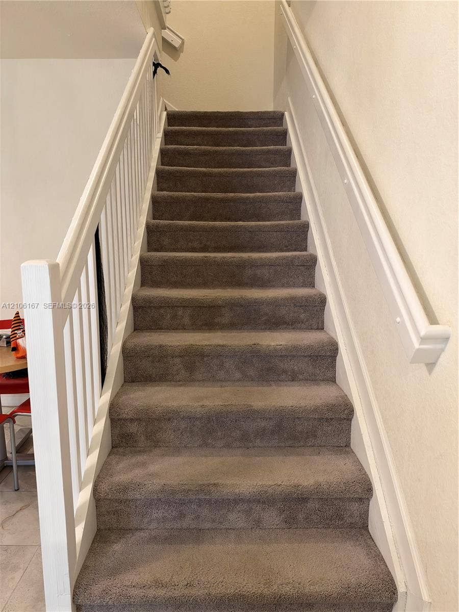 3277 W 100th Terrace, Hialeah, FL 33018 Staircase featuring neutral-toned carpeting, white painted vertical balusters, and a matching handrail
