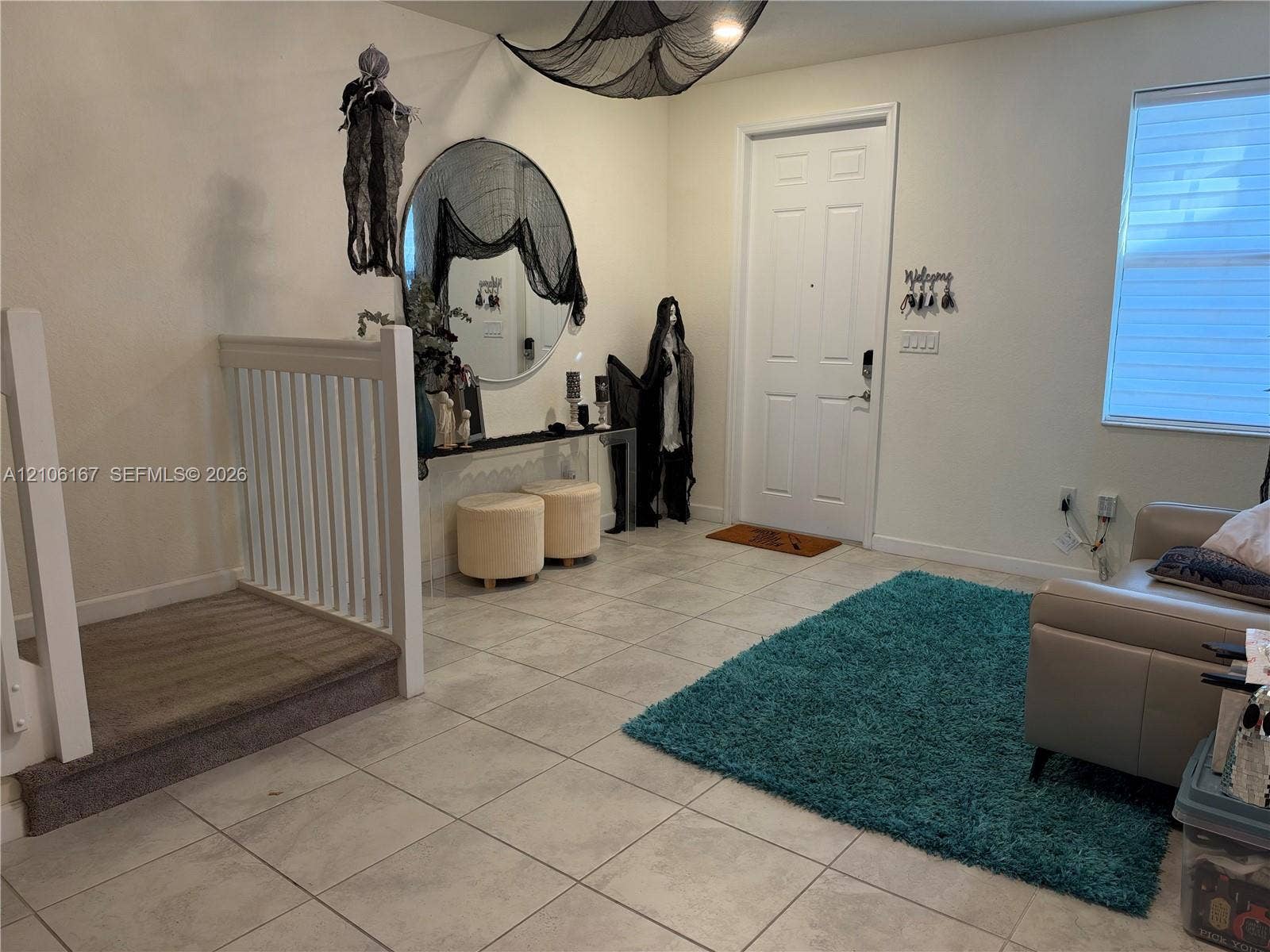 3277 W 100th Terrace, Hialeah, FL 33018 Interior space featuring large-format ceramic tile flooring, a recessed entryway with a white paneled door, and a built-in wooden stair railing with white balusters