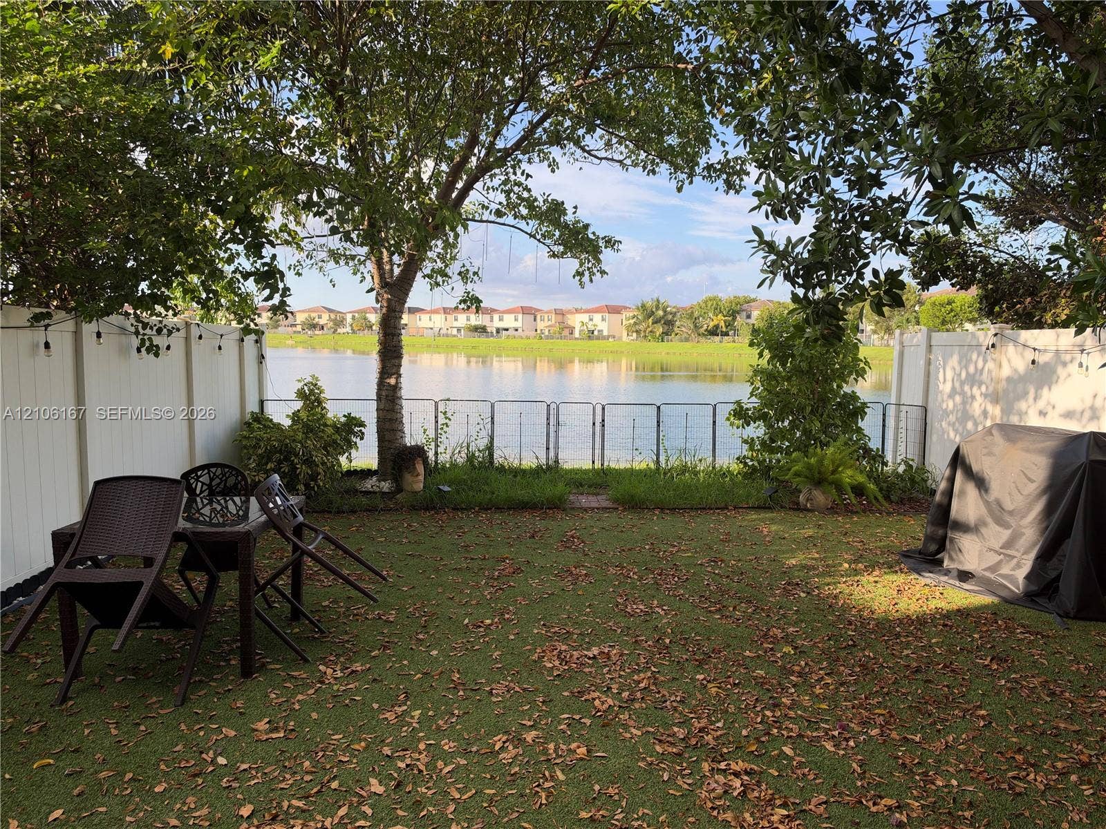 3277 W 100th Terrace, Hialeah, FL 33018 Backyard featuring a waterfront location, white vinyl privacy fencing, mature trees, and a metal perimeter fence