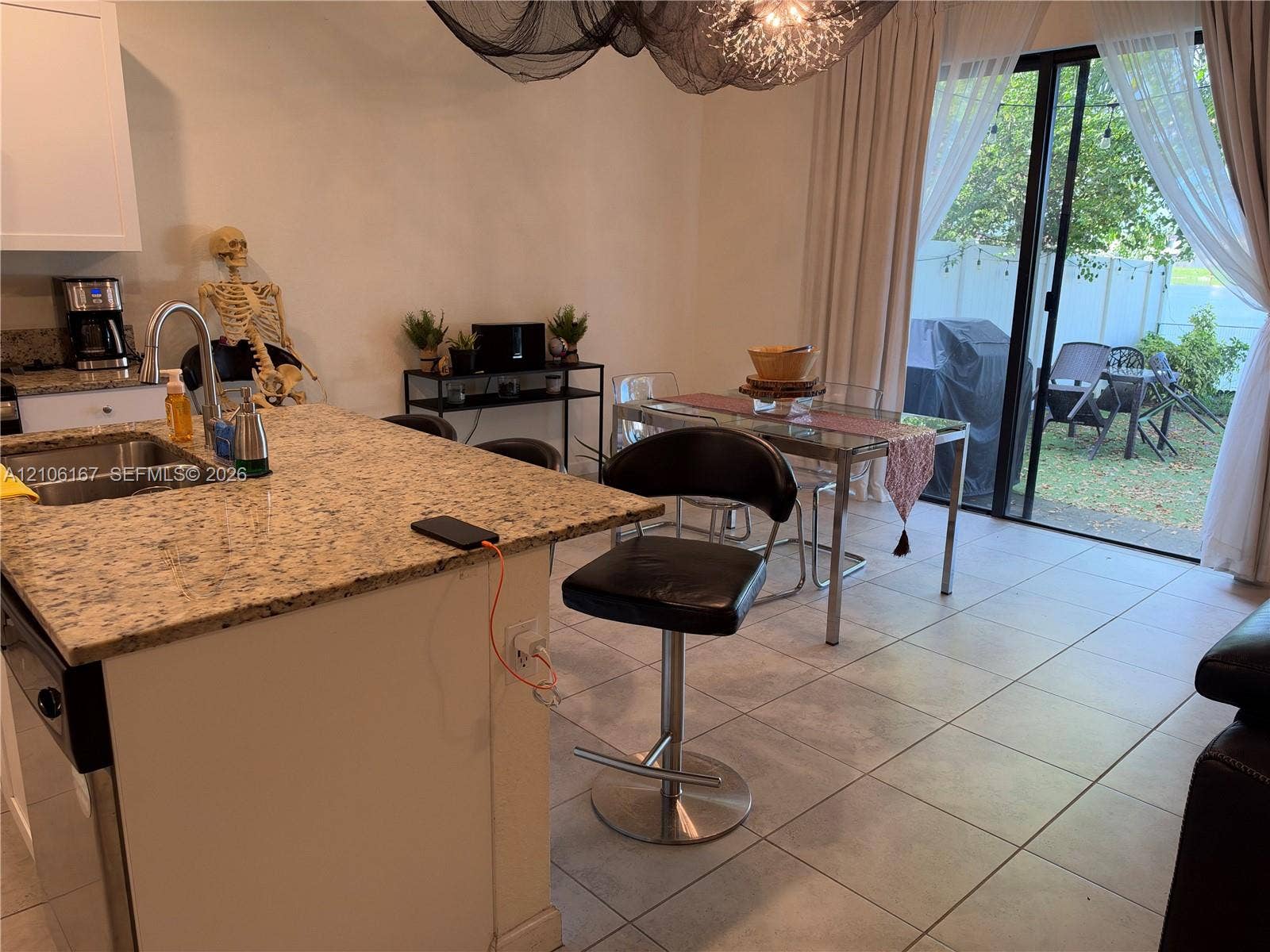 3277 W 100th Terrace, Hialeah, FL 33018 Kitchen featuring a speckled stone countertop, stainless steel dual-basin undermount sink, white cabinetry, ceramic tile flooring, and a large sliding glass door