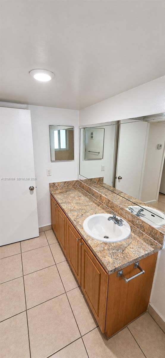 10820 SW 200th Drive, #162, Cutler Bay, Cutler Bay, FL 33157 Vanity featuring wood-finish cabinetry, a stone-patterned countertop, an integrated circular sink, a full-width wall mirror, and neutral floor tiling