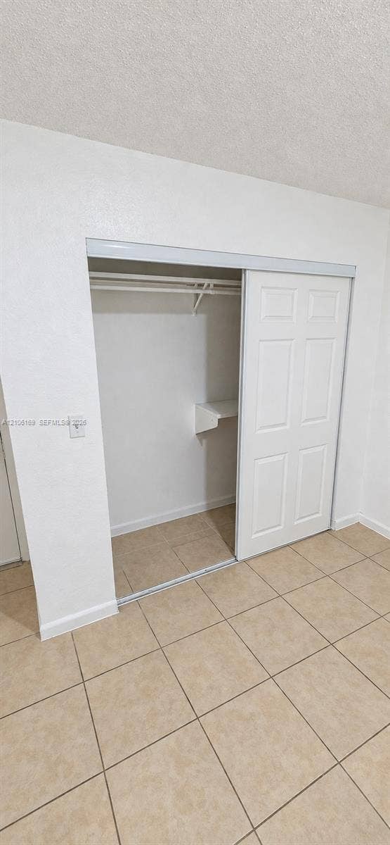 10820 SW 200th Drive, #162, Cutler Bay, Cutler Bay, FL 33157 Closet featuring dual sliding six-panel doors, integrated shelving, and a hanging rod, finished with neutral tile flooring
