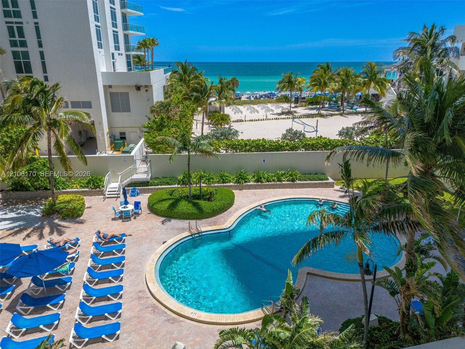 4001 S Ocean Drive, #12B, Hollywood, Hollywood, FL 33019 Curved swimming pool with stone-tiled decking, mature palm landscaping, and concrete perimeter wall