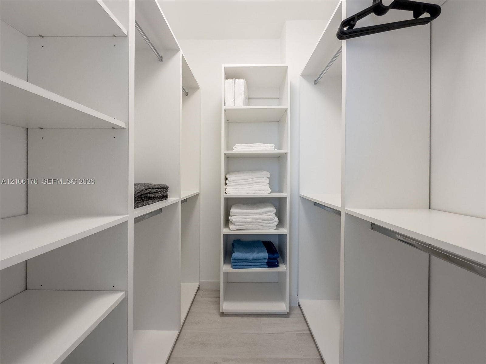 4001 S Ocean Drive, #12B, Hollywood, Hollywood, FL 33019 Walk-in closet featuring white floor-to-ceiling built-in cabinetry, multiple adjustable shelving tiers, integrated hanging rods, and wood-finish flooring
