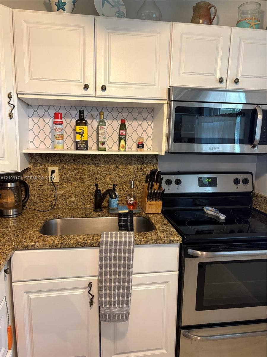 White shaker-style cabinetry, stone-finish countertops, stainless steel appliances, stainless steel undermount sink with high-arc faucet, and decorative patterned backsplash