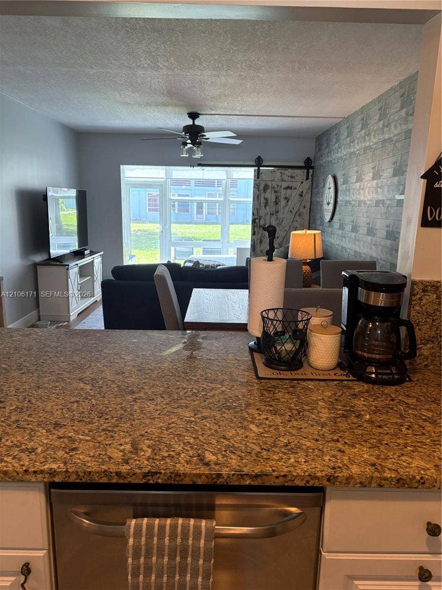 Kitchen featuring a stone-composite countertop, stainless steel dishwasher, white cabinetry, decorative textured wall finish, and a ceiling fan