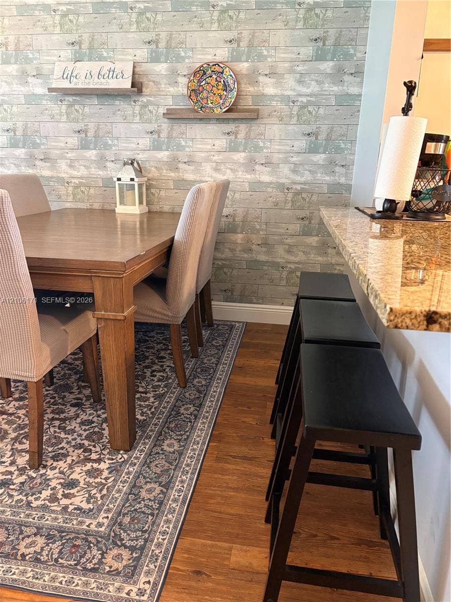 Wood-finish flooring, stone-finish breakfast bar countertop, and decorative wall treatment featuring a horizontal plank pattern