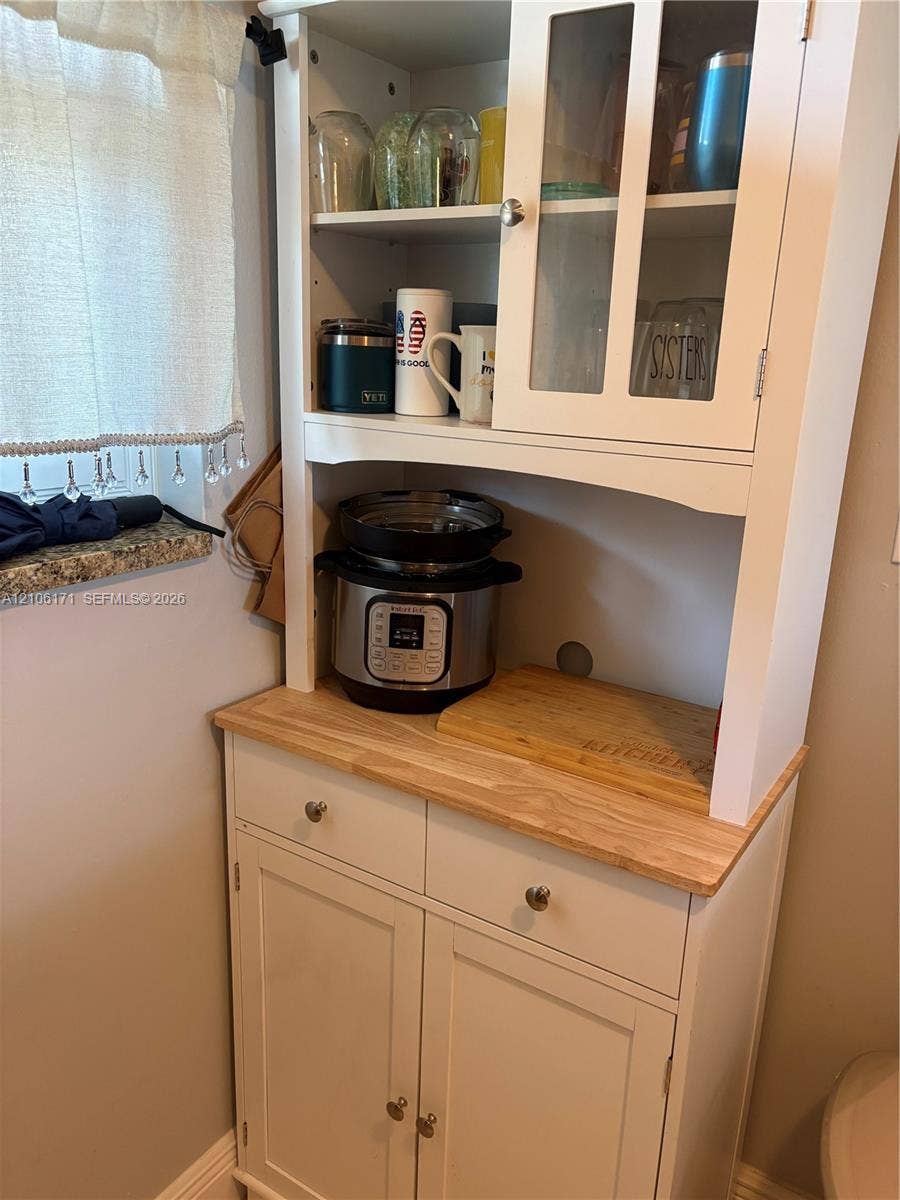 Built-in white hutch featuring upper glass-paneled cabinetry, a natural wood countertop, and lower cabinet storage with brushed metal hardware
