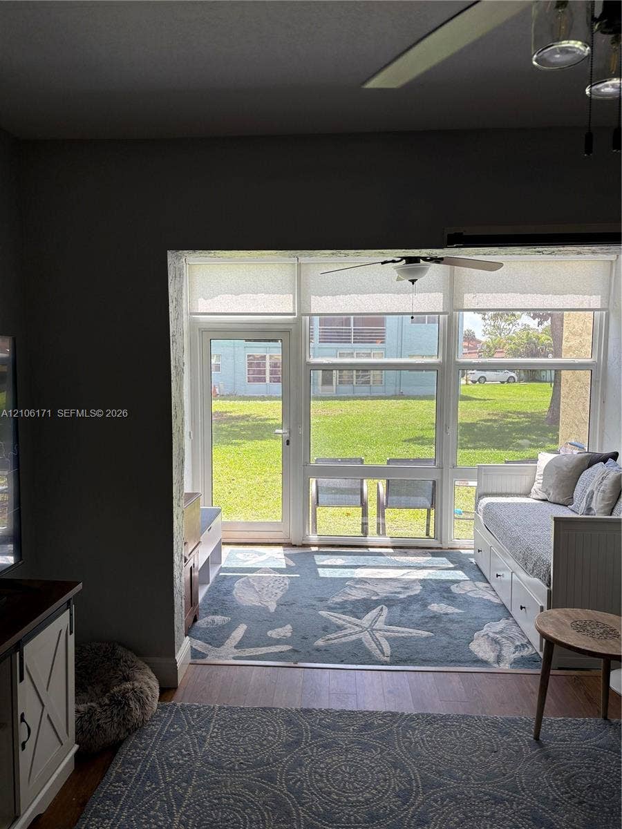 Enclosed area featuring multi-pane window walls, a glass-panel door, wood-finish flooring, and a ceiling fan