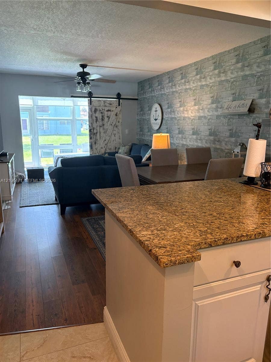 Kitchen featuring a stone-look countertop, wood-finish flooring, a sliding barn door, a ceiling fan with light fixture, and an accent wall with patterned finish