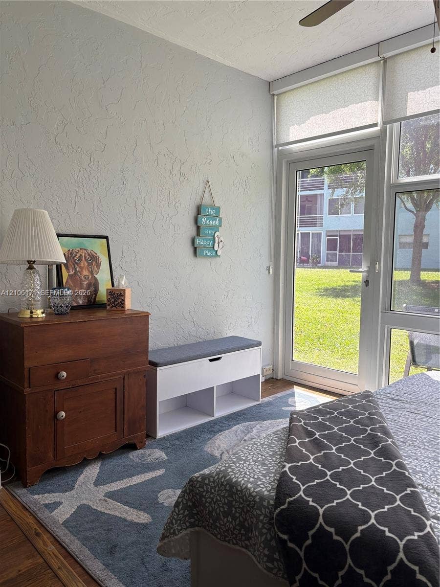 Floor-to-ceiling glass paneling and full-length glass door providing outdoor access, textured wall surfaces, and wood-finish flooring