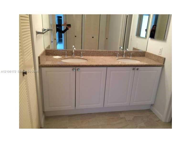 20515 E Country Club Drive, #246, Aventura, Aventura, FL 33180 Dual vanity featuring a neutral-toned stone countertop, white cabinetry with silver-tone hardware, undermount sinks, and wall-to-wall mirror